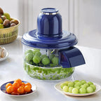 Blue manual food chopper with green grapes inside, surrounded by fresh produce on kitchen counter