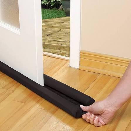 Black door draft stopper being placed on wooden floor to block gaps under door